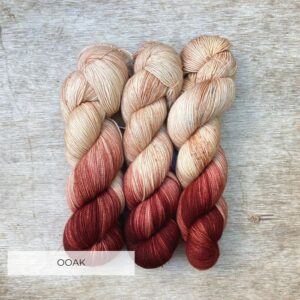 Three skeins of sock yarn in a pinky cream colour, lightly speckled and with one end of the skein dipped in a dark red