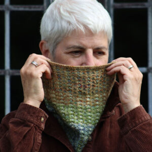 A woman wearing a brown corduroy shirt peaks out from behind a knitted cowl