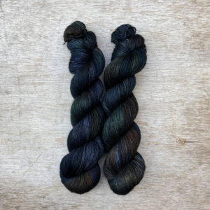 Two skeins of inky blue yarn with splashes of bottle green and rust