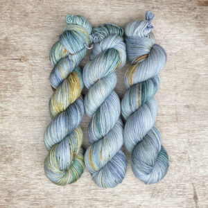 Three skeins of plump DK wool in shades of light blue and green with gold splashes