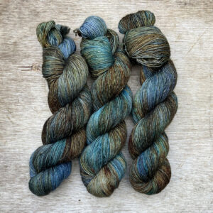 Three skeins of merino and linen in a mid blue green with splashes of golden brown