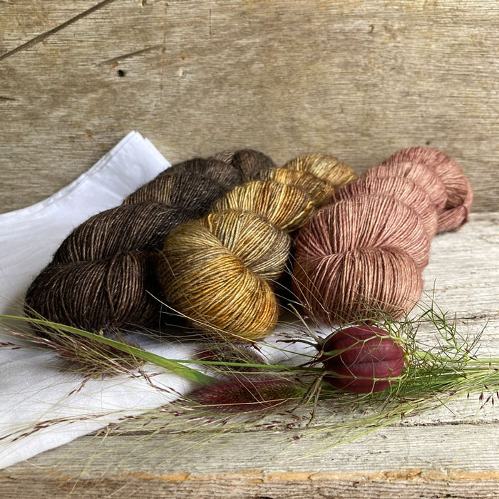 Three skeins of merino and linen in a pink a golden grey and a dark brown