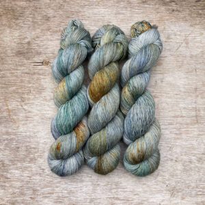 Three skeins of merino and linen in a mid blue green with splashes of golden brown