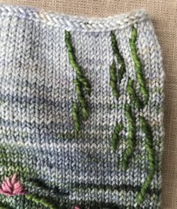Stem stitch worked in green wool on blue knitted mitten