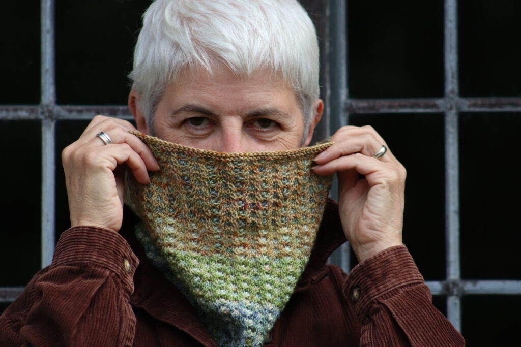 A woman wearing a brown corduroy shirt peaks out from behind a knitted cowl