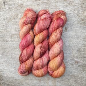 Three skeins of Classic Sock in peach, coral and mulberry freckled with terracotta and gold