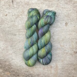 Two skeins of Classic Sock in pale green with splashes of moss , turquoise, gold and indigo