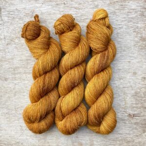 Three skeins of a wool and linen blended yarn in a golden mustard