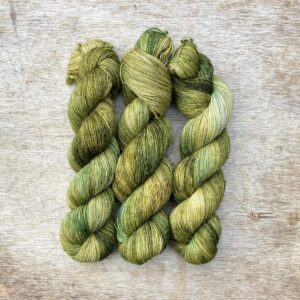 Three skeins of a wool and linen blended yarn in green with splashes of cream and flecks of gold