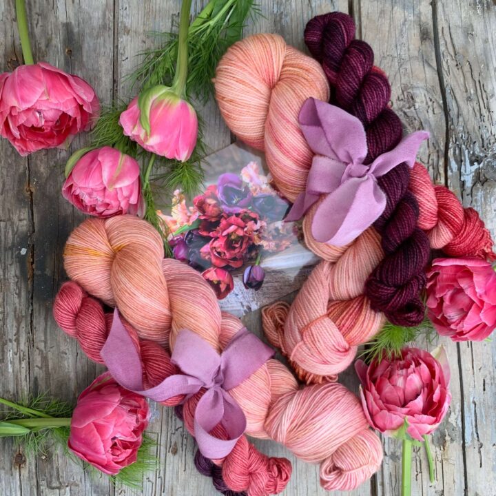 Two bundles of pink and purple yarn tied with ribbon and surrounded with tulips