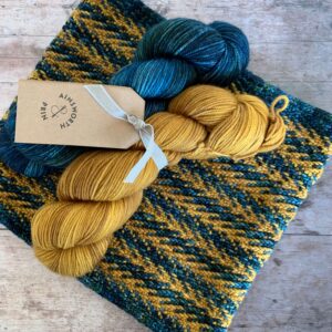 Slipped Stitch knitted cowl with dark green and gold skeins of yarn