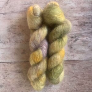 Two skeins variegated yellow, green & cream mohair silk yarn on pale wood background.