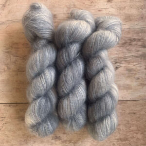 Three skeins of pale blue/grey mohair and silk yarn on pale wood background