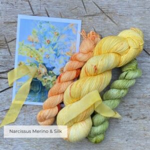 A skein of daffodil yellow sock yarn with two coordinating minis in green and apricot with the card that inspired them