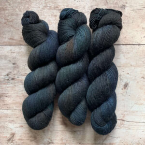 Three skeins classic sock in blue/black on pale wood surface