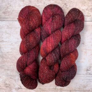 Three skeins of Merino and linen yarn in a rich red and dark pink