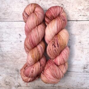 Mid mid pink variegated Plump sock yarn on a cream base with darker speckles. Sat on wood background
