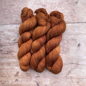 Three skeins of, rich ginger silky yarn on wood background
