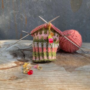 An ice lolly stitch marker on on some stripy knitting with a small pile of jewel like markers in front
