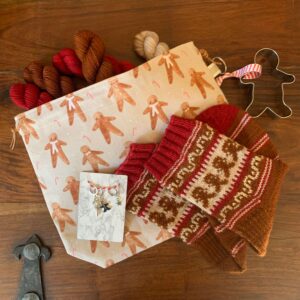 A folded pair of I'm a gingerbread man socks on a themed workbag with coordinating stitch markers a biscuit cutter and yarn
