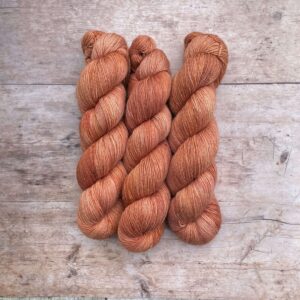 Three skeins pale terracotta silk yarn on wood background
