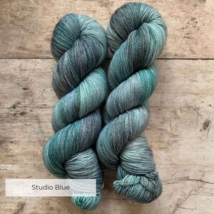 Two skeins classic sock in shades of blue, grey and turquoise on pale wood surface