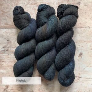 Three skeins classic sock in blue/black on pale wood surface