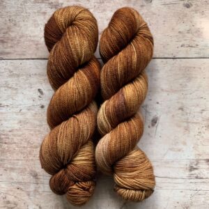 Two skeins classic sock in caramel browns and cream on pale wood surface
