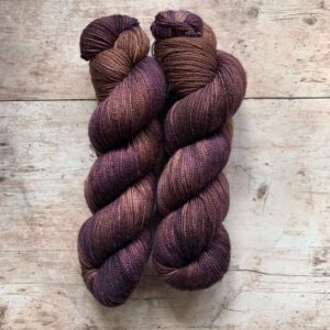 Two skeins classic sock in plum and tan on pale wood surface