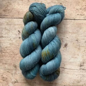 Two skeins classic sock in mid blue and teal with tan speckles on pale wood surface