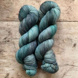 Two skeins classic sock in shades of blue, grey and turquoise on pale wood surface