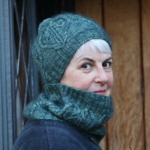 Woman in blue Heart's End bobble hat and cowl against a wooden door