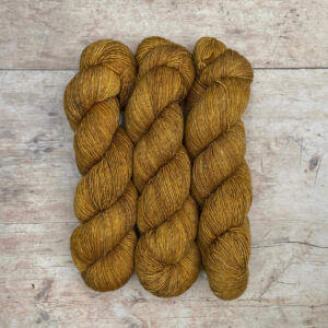 Three skeins of a wool and linen blended yarn in a golden mustard