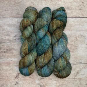 Three skeins of merino and linen in a mid blue green with splashes of golden brown