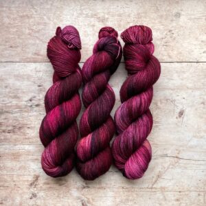 Three skeins classic sock in pink, plum and lilac on pale wood surface