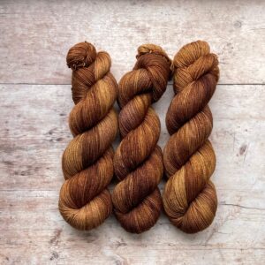 Three skeins classic sock in caramel browns and cream on pale wood surface