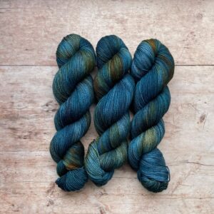 Three skeins classic sock in mid to dark blue with orange variegation on pale wood surface