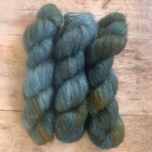 Three skeins of mid blue and rust variegated mohair and silk lace weight yarn on pale wood background