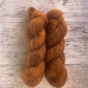 Three skeins of rusty brown mohair and silk lace yarn on pale wood background