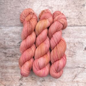 Three skeins of Plump Sock Yarn in shades of Pink on pale wood background