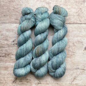 Three skeins of silk merino yarn in shades of blue on wood background