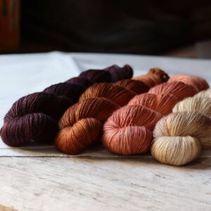 Four skeins of Merino & Silk wool in a deep aubergine, rust, coral and cream on a linen and wood background