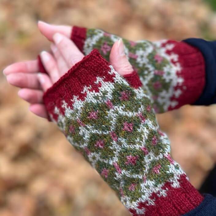 A pair of woman's hands wearing red, green and cream colour work gloves in Shetland wool.