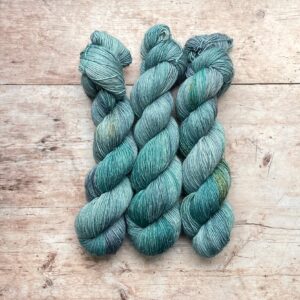 Three skeins Flax in shades of blue, grey and turquoise on pale wood surface