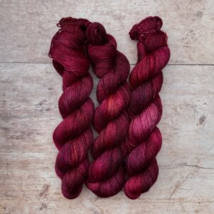 Three skeins Merino Floof in pink, plum and lilac on pale wood surface