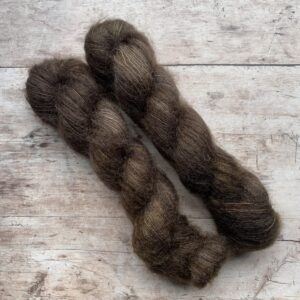 Two skeins of mohair and silk lace weight yarn in bitter chocolate on pale wood background