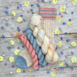A full skein of Classic Sock in pastel cream, pink and blue with toffee coloured speckles with a small skeins of coordinating pink and blue on a sock knitted in the same colours