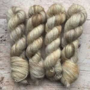 Four skeins of pale creamy, taupe mohair and silk lace weight yarn on pale wood background