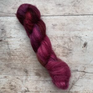 One skein of mohair and silk lace weight yarn in pink, plum and lilac on pale wood background
