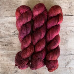 Three skeins of, rich pink, magenta and raspberry variegated merino mohair yarn on wood background